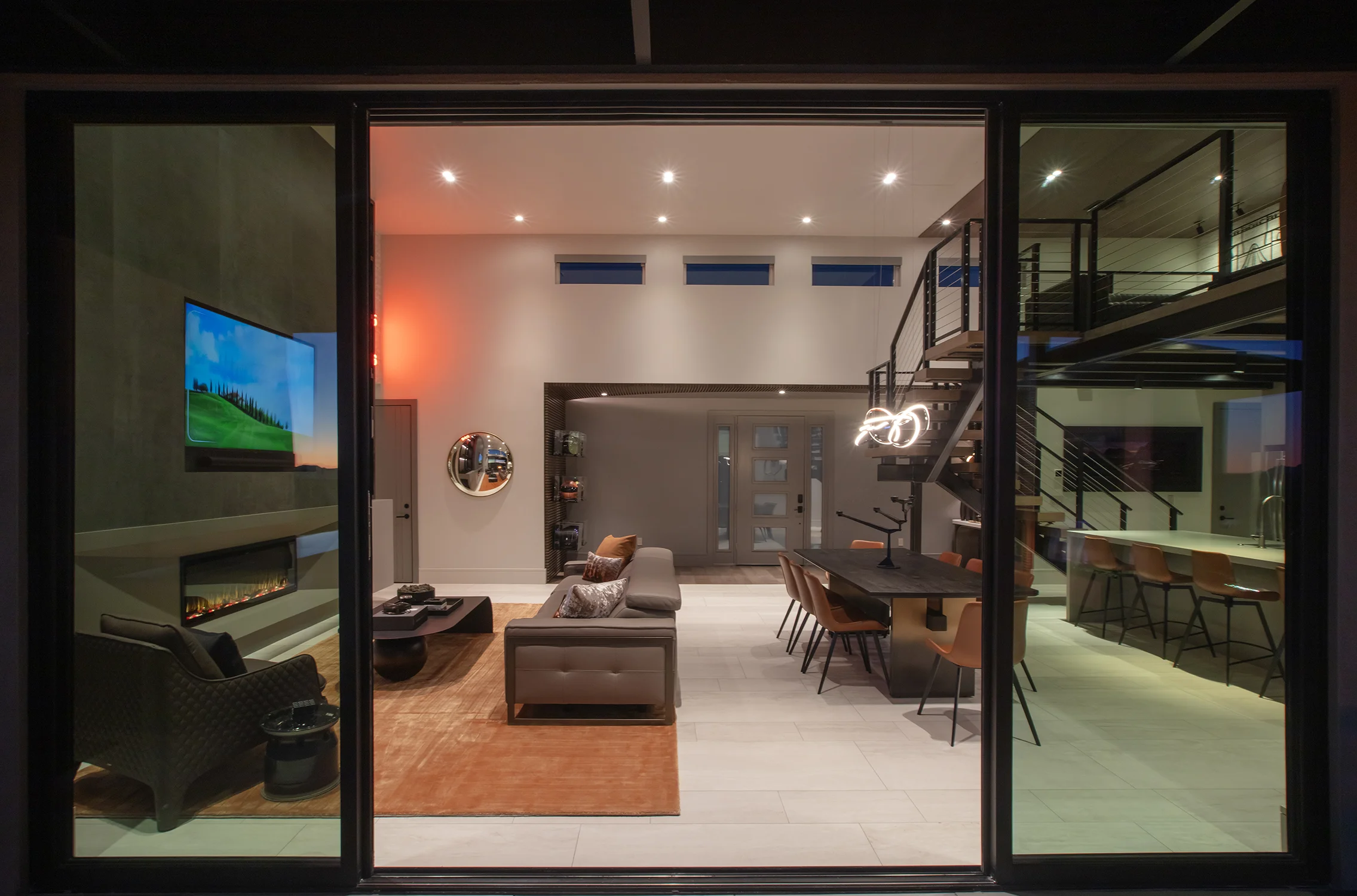 Open-plan living and dining room with a floating staircase, seen through sliding glass doors at dusk